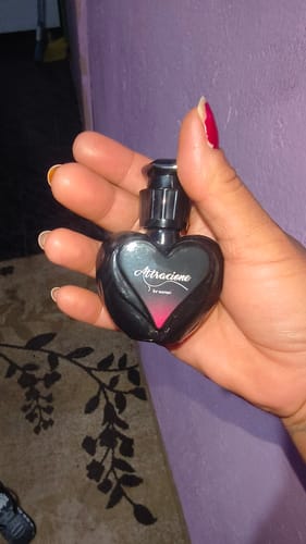 Reviewer's hand holding a small black heart-shaped Attracione perfume bottle