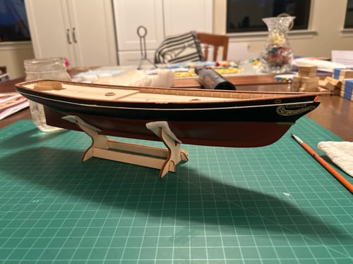 Customer's America 1851 model yacht kit on a wooden stand, set on a green cutting mat.