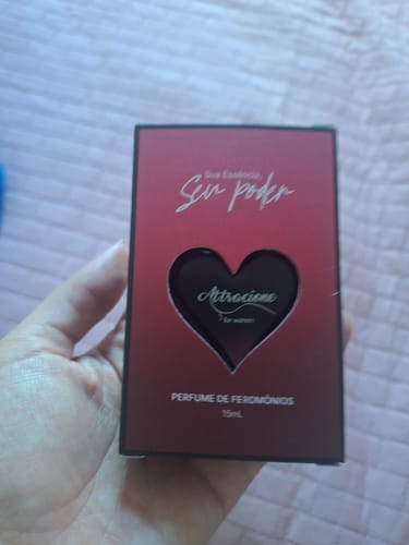 Customer's hand holding the box of Perfume Attracione Sensual, featuring a red gradient and heart-shaped cutout.