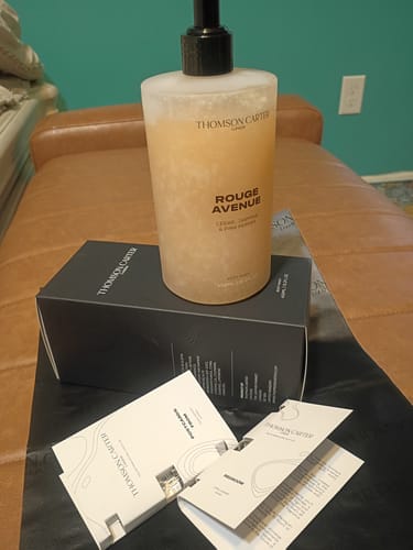 Customer's Rouge Avenue body wash pump bottle, black box, and product info cards on a leather surface.
