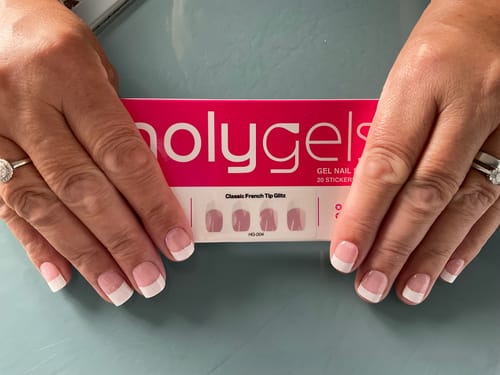 Customer's hands displaying manicured nails next to a package of HolyGels classic french tip glitz stickers.