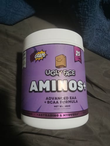 Customer's purple tub of UGLYFACE AMINOS+ grape flavor powder on a fabric surface.