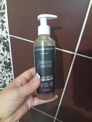 Customer's hand holding a 200ml bottle of Sebovia Essence shampoo in a tiled bathroom.