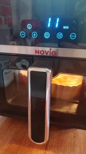 Reviewer's Novio StonePro air fryer in operation, displaying a blue 11-minute timer on the digital control panel