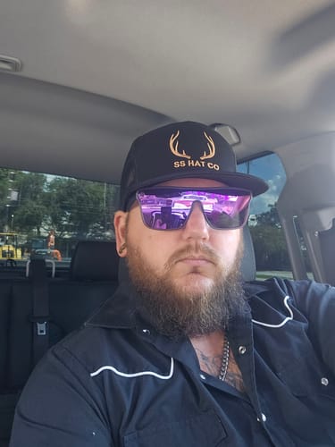 Customer's Hat of the Month Crew cap with antlers logo, worn by a bearded reviewer inside a vehicle.