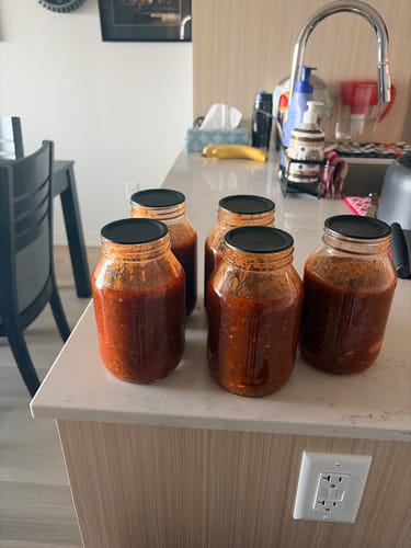 Customer's Chalkboard Top Mason Jar Lids used on four glass jars filled with red sauce on a kitchen counter.