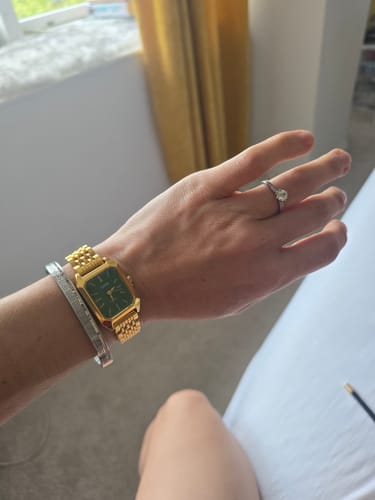Reviewer's gold Claire De Mains watch with a green face worn on their wrist with a silver bracelet.