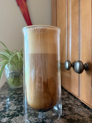 Customer's FLUR iced coffee glass filled with a layered latte, sitting on a dark kitchen counter.