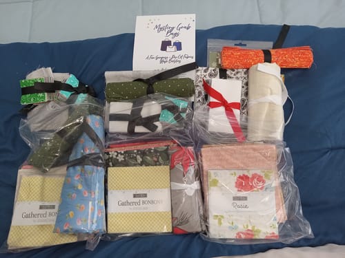 Customer's haul of Mystery Grab Bag fabric bundles including various colorful precut pieces and charm packs.