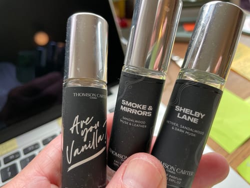 Customer's hand holding three Are You Vanilla perfume vials with black labels against a laptop screen background.