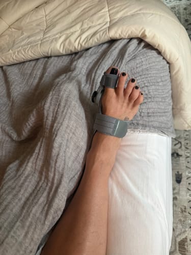 Customer's gray Treatmedy Bunion Fix on their foot while lying in bed.