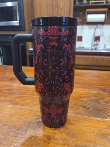 Customer's red and black lace-patterned Thicc Buddy mug with handle, standing on a wooden table.