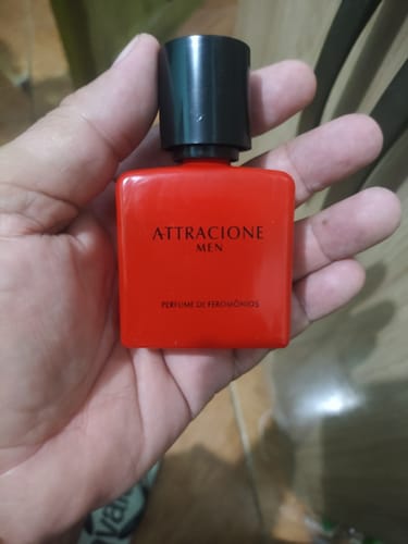 Customer's hand holding a square red Attracione Men perfume bottle with a black cap.
