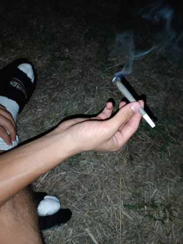 Reviewer's hand holding a lit THC-A Pre-Roll Cali Blend cone outdoors at night, with wisps of smoke visible.