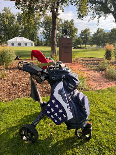 Customer's dark blue Cybercart electric golf caddy with a bag on a lush green golf course.