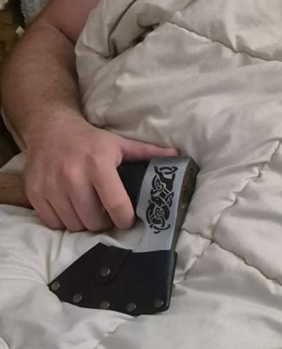 Customer's hand holding a custom engraved viking-style axe with decorative carvings while lying in bed.