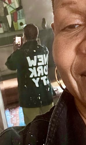 Customer's mirror selfie wearing the black denim 'NYC' Painted Jacket with white text on the back.
