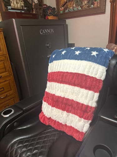 Reviewer's soft Hugs Flag Blanket with red, white, and blue pattern draped over a black leather chair.