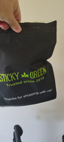 Customer's black shipping bag with green Sticky Green logo being held by a person.