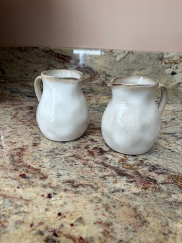 Customer's pair of Crema Organic Creamer Pitchers with a rounded, white stoneware form sitting on a granite countertop.
