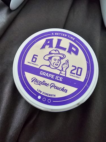 Customer's purple ALP Grape Ice nicotine pouch tin, showing 6mg strength and 20 pouch count, resting on dark fabric.
