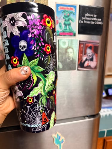 Customer's hand holding a Toxic Bloom To-Go Buddy tumbler with colorful floral and skull patterns.
