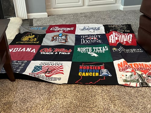 Customer's Project Repat T-Shirt Quilt laid out on a carpet, featuring various colorful cotton squares with logos.