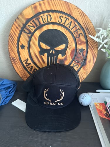 Customer's black Hat of the Month Crew cap with gold deer antlers logo, sitting on a desk.