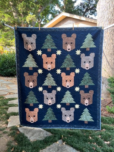 Customer's Midnight Pines quilt hanging outdoors, featuring a dark blue pattern with brown bears and green pine trees.