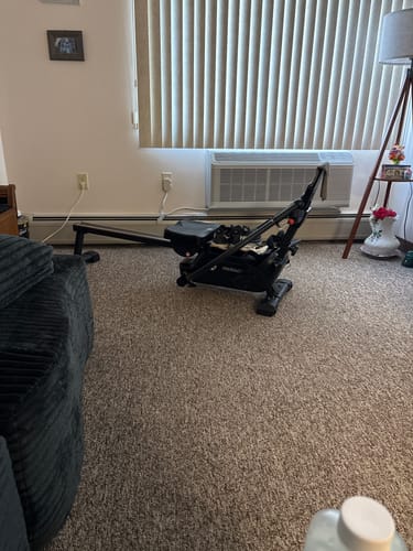 Customer's black NovaRow RS3 rowing machine set up on carpet in a home living room.