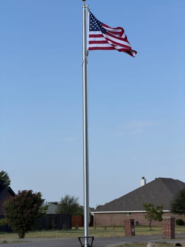 Customer's 20 ft. Commercial Flagpole with an American flag against a clear blue sky in a residential area.