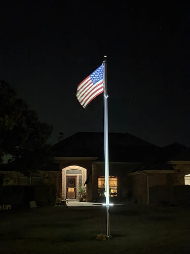 Customer's 20 ft. Commercial Flagpole illuminated at night with an American flag flying in a residential yard.