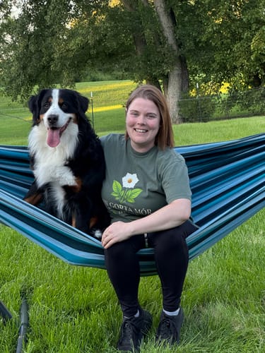 Customer's olive green An Gorta Mór T-Shirt with floral design, worn by reviewer in a hammock with a dog.
