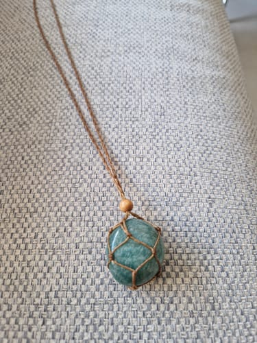 Customer's green Amazonite pierre roulée held in a brown knotted cord necklace, resting on a textured fabric surface.