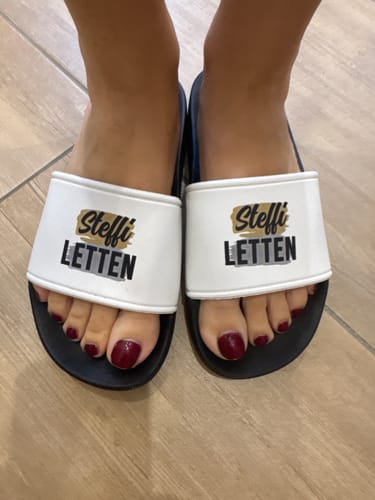 Reviewer's personalisierte Badeschlappen mit dem Namen Steffi Letten an den Füßen, getragen auf einem hellen Boden.