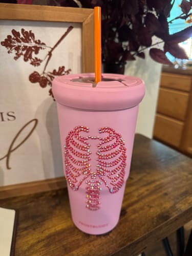 Customer's pink To-Go Buddy cup featuring a sparkly skeleton rib cage design, sitting on a wooden surface.