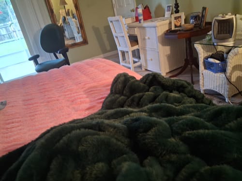 Customer's plush dark green Hugs Pine blanket draped over a bed in a cozy bedroom.