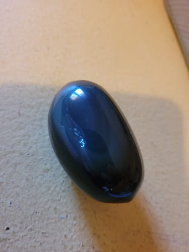 Customer's smooth, dark obsidian pebble with subtle iridescent reflections, captured in a close-up shot.