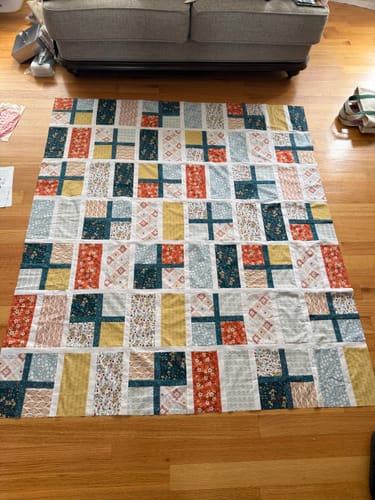Reviewer's finished Apple Cider Sew-Ready Quilt Kit laid out on a wooden floor, featuring autumn-toned fabric patches.