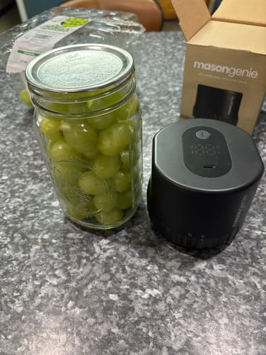 Customer's black Mason Genie vacuum sealer beside a jar of fresh green grapes and the product's cardboard packaging.