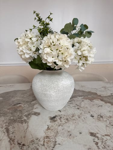 Customer's Eucalyptus & White Hydrangea arrangement in a textured white vase on a marble table.