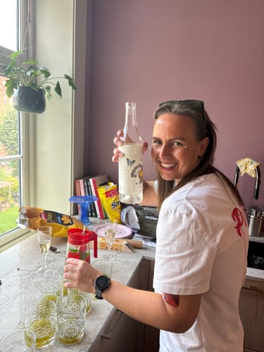 Reviewer in a kitchen setting with Artisan Oak kontaktplast on the surface, holding a bottle during a celebration.