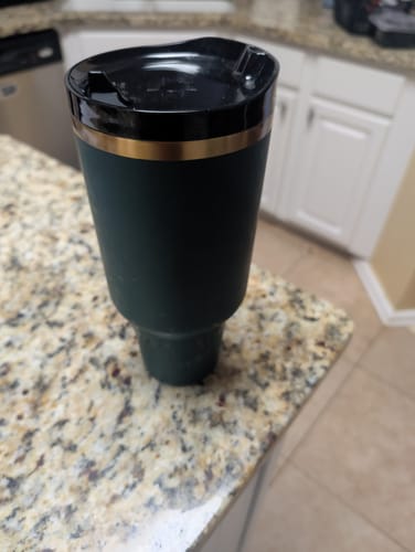 Customer's dark green Thicc Buddy tumbler with a black lid, sitting on a speckled kitchen countertop.