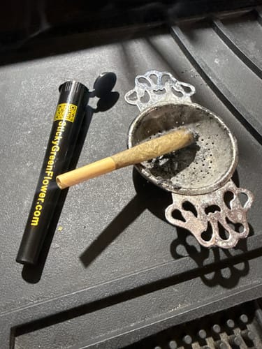 Customer's Colombia Gold pre roll resting on an ornate metal ashtray next to a black storage tube.