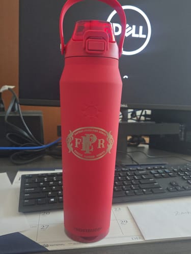 Customer's custom red water bottle with a gold F-P-R emblem, sitting on an office desk.