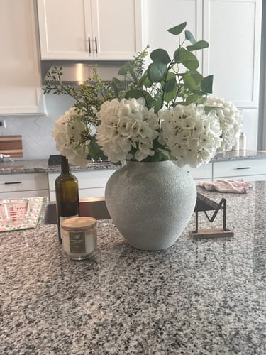 Customer's Eucalyptus & White Hydrangea arrangement in a round grey vase on a kitchen counter.