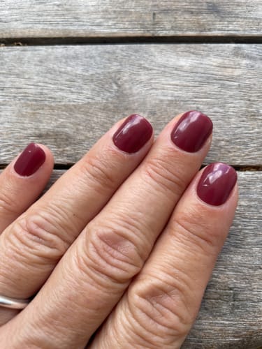 Customer's hand showing Royal Temptation UV Gel Nail Wraps in a deep wine-red color on a wooden background.