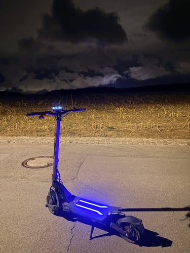 Customer's Ausom L2 Max e-scooter parked on road at night, illuminated by glowing blue lights against a dark landscape.
