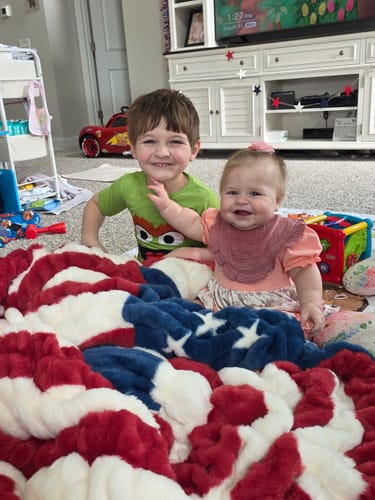 Customer's children smiling on the soft, patriotic Hugs Flag Blanket.