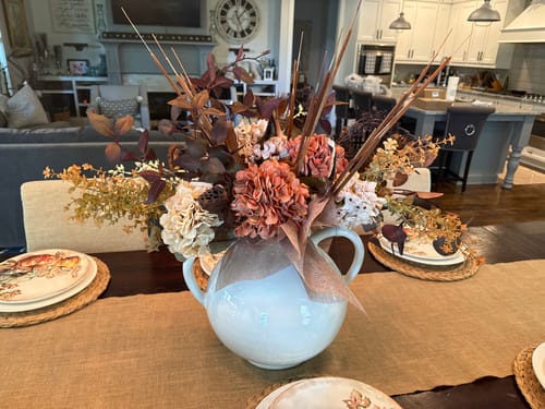 Customer's orange hydrangea and eucalyptus faux arrangement in a light blue vase on a dining table.